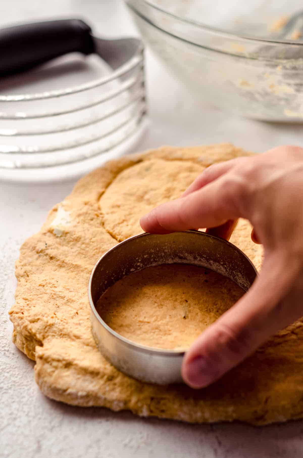 hand using a cookie cutter to cut pumpkin biscuit dough into circles