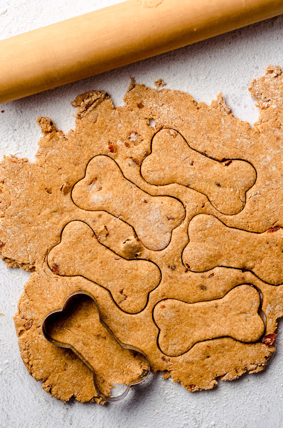 dough for homemade dog treats being cut with a bone cookie cutter