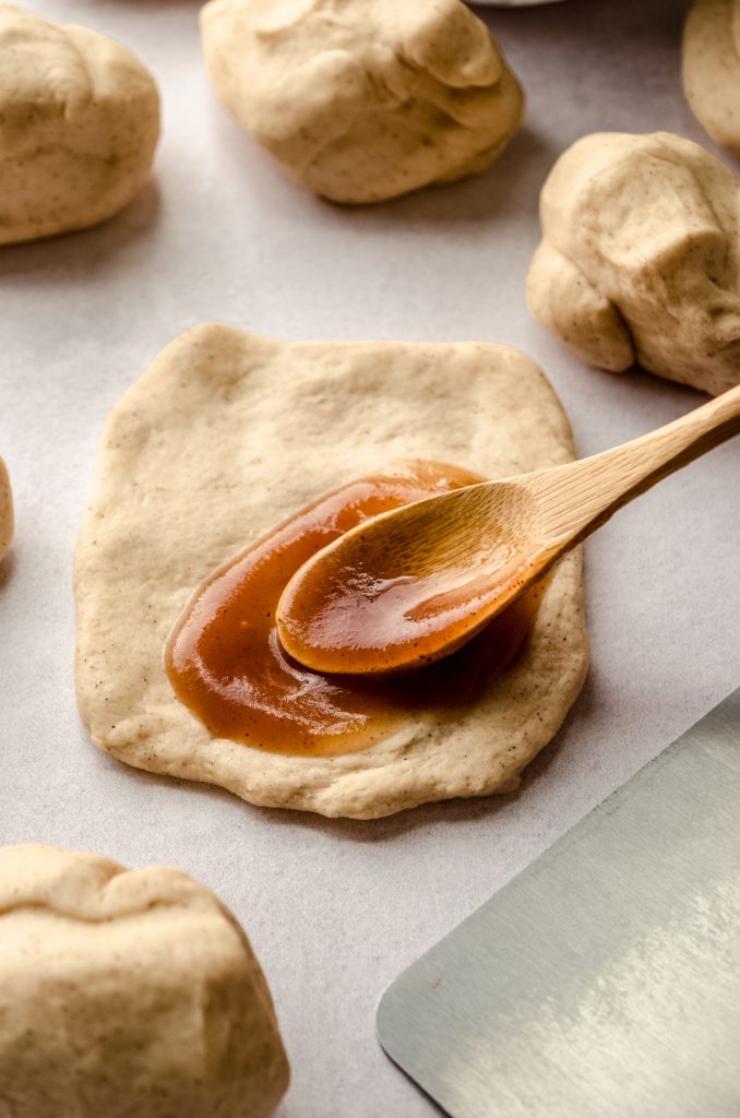 Someone is using a wooden spoon to spread apple butter onto a disc of dough to make apple butter pull-apart bread.