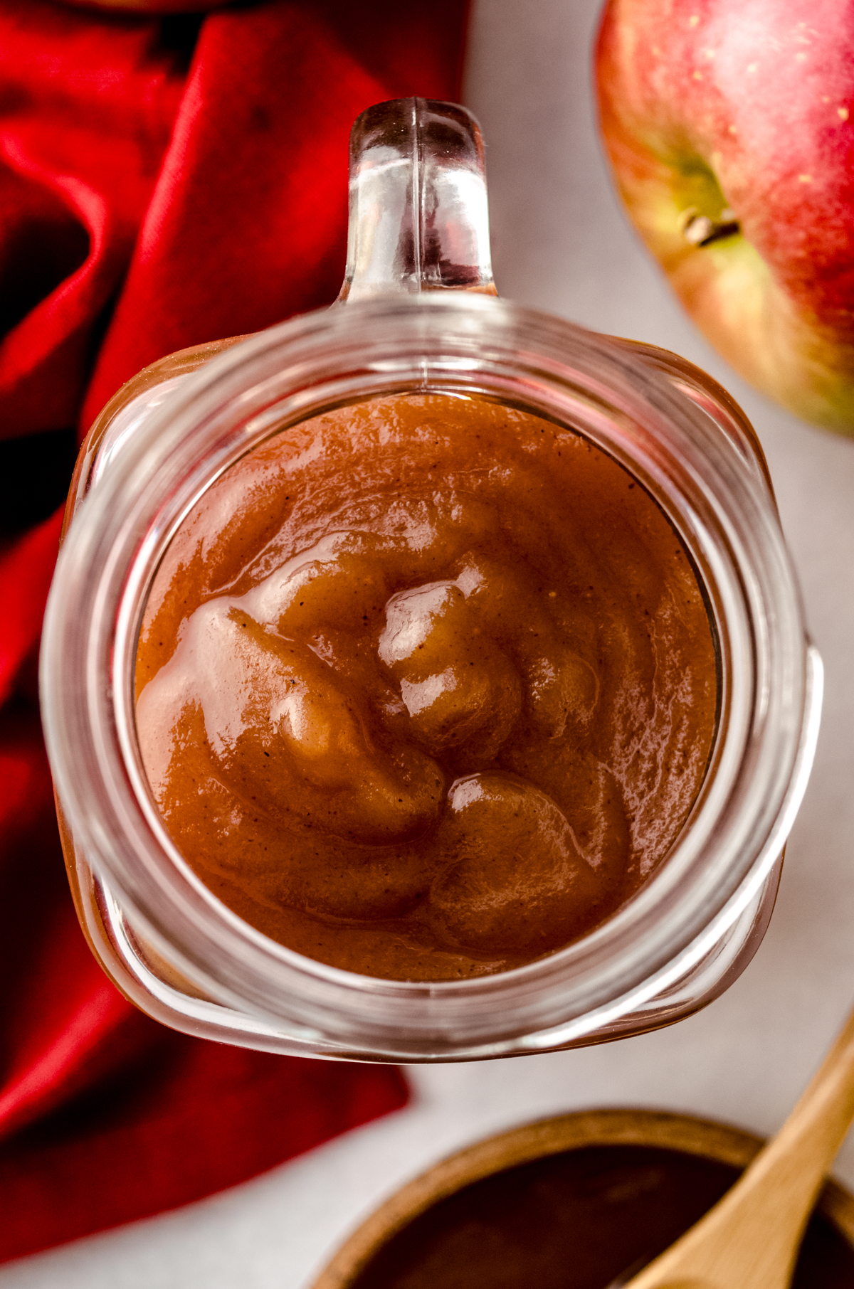 Aerial photo of a jar of homemade apple butter with apples and a bowl of apple butter around it.