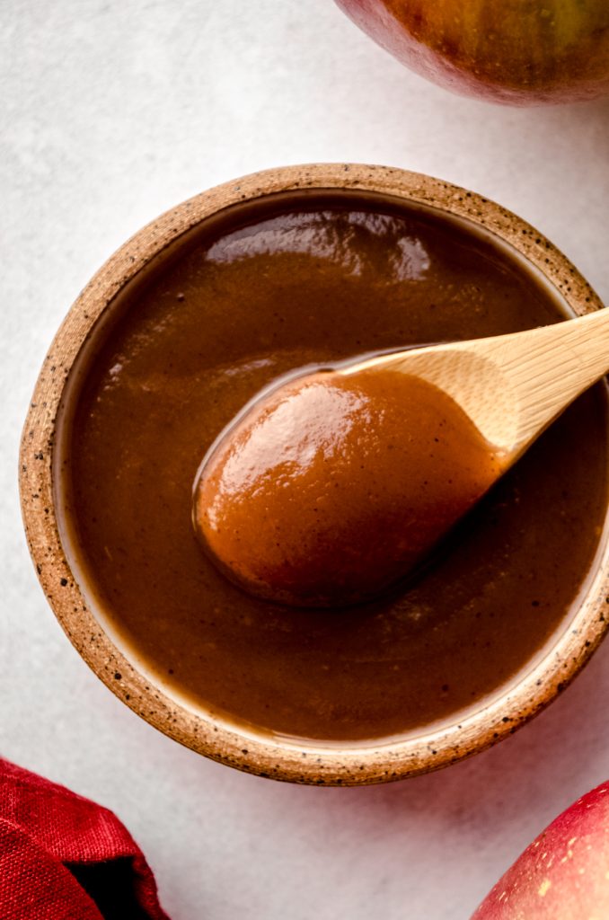 Aerial photo of apple butter in a small bowl and a wooden spoon scooping some of it out.