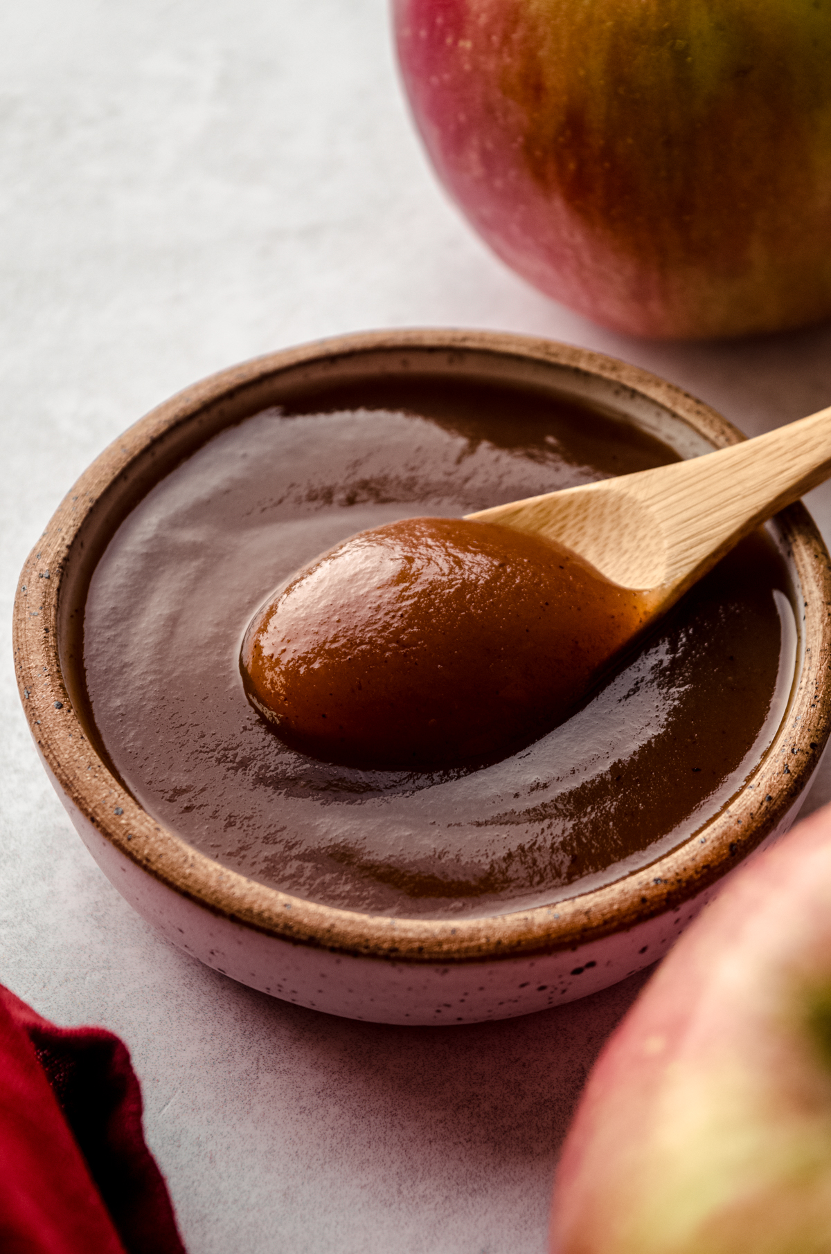 Apple butter in a small bowl and a wooden spoon scooping some of it out.