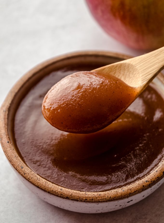 Apple butter in a small bowl and a wooden spoon scooping some of it out.