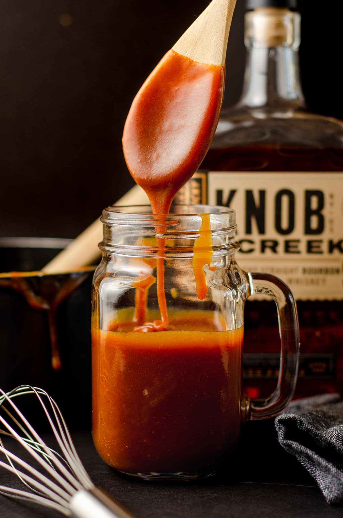 a wooden spoon in a glass jar of salted bourbon caramel sauce