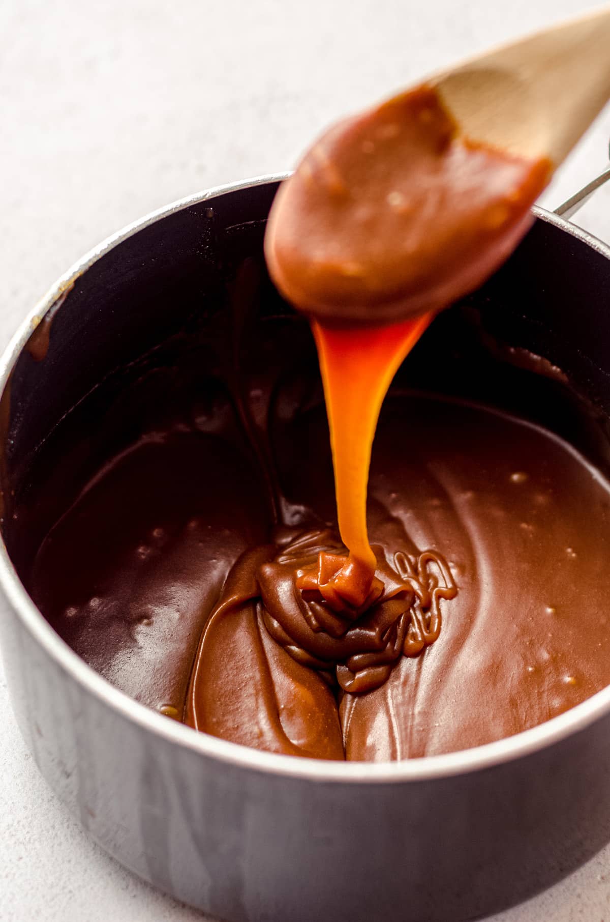 wooden spoon dipped into a bourbon saucepan of salted caramel sauce and dripping it back into the pan