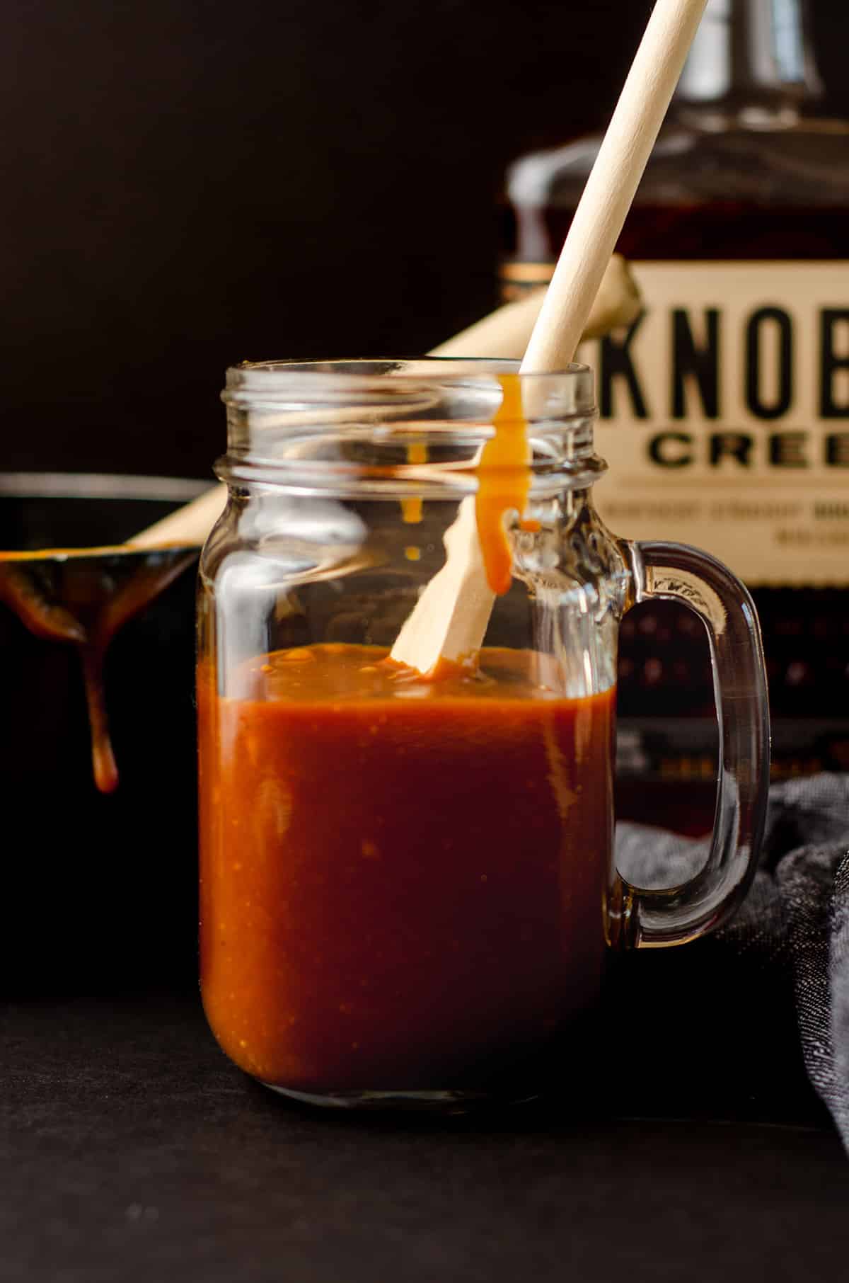 a wooden spoon in a glass jar of salted bourbon caramel sauce