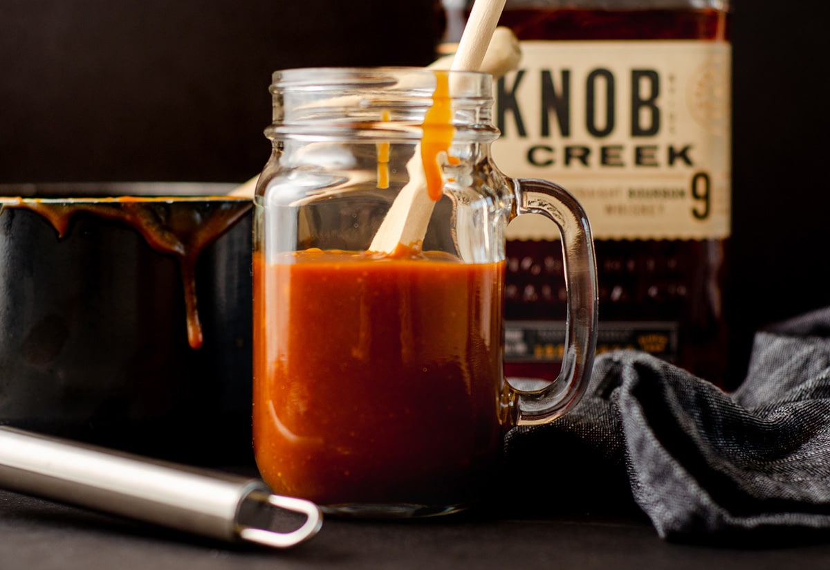 a wooden spoon in a glass jar of salted bourbon caramel sauce