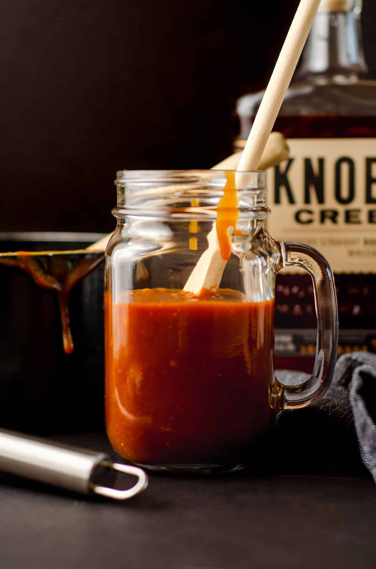 a wooden spoon in a glass jar of salted bourbon caramel sauce