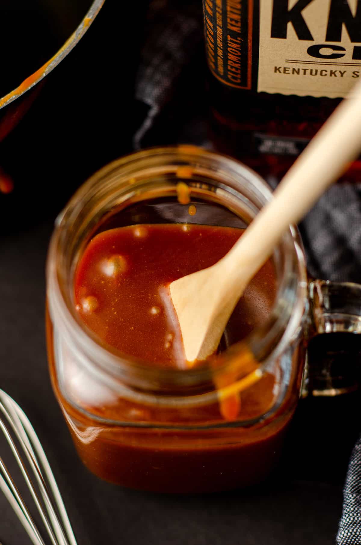 a wooden spoon in a glass jar of salted bourbon caramel sauce