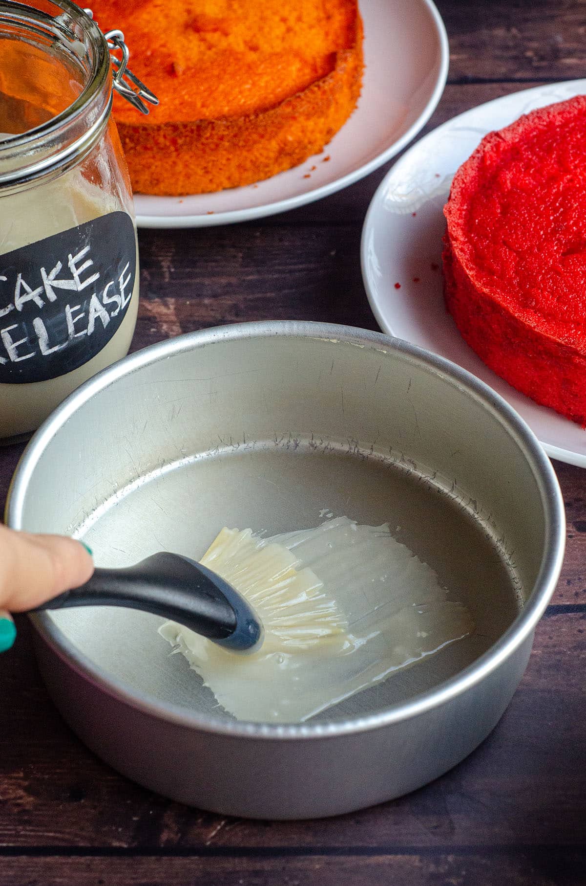 A hand brushing homemade cake release into a cake pan with a pastry brush.