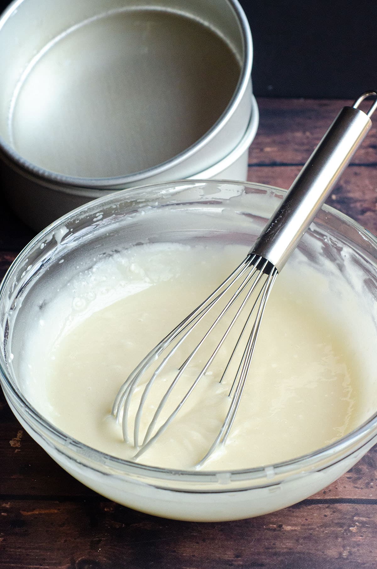 Homemade cake release in a glass bowl with a whisk and cake pans in the background.