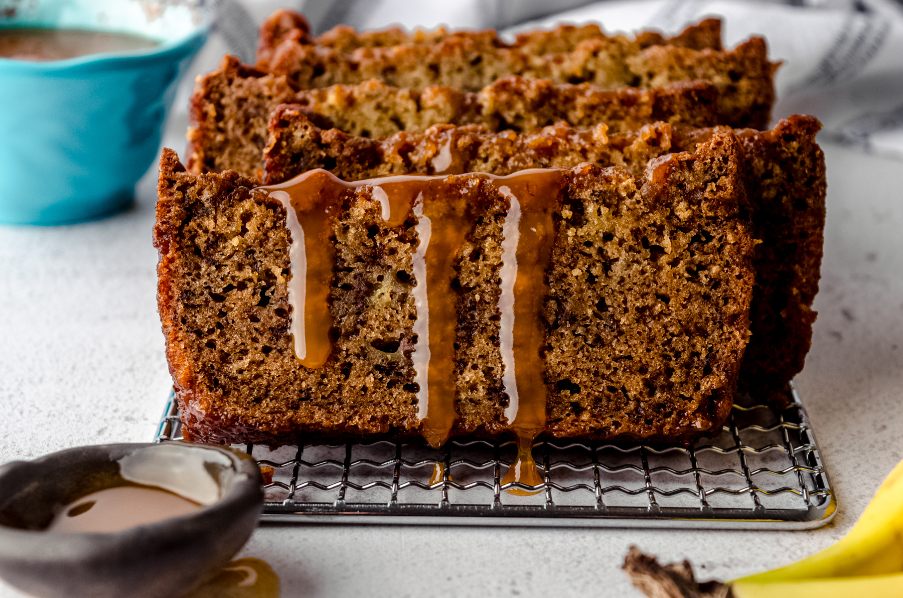 Slices of salted caramel banana bread on a cooling rack with caramel dripping down the slice in the front.