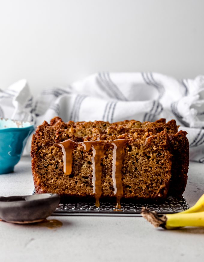 Slices of salted caramel banana bread on a cooling rack with caramel dripping down the slice in the front.