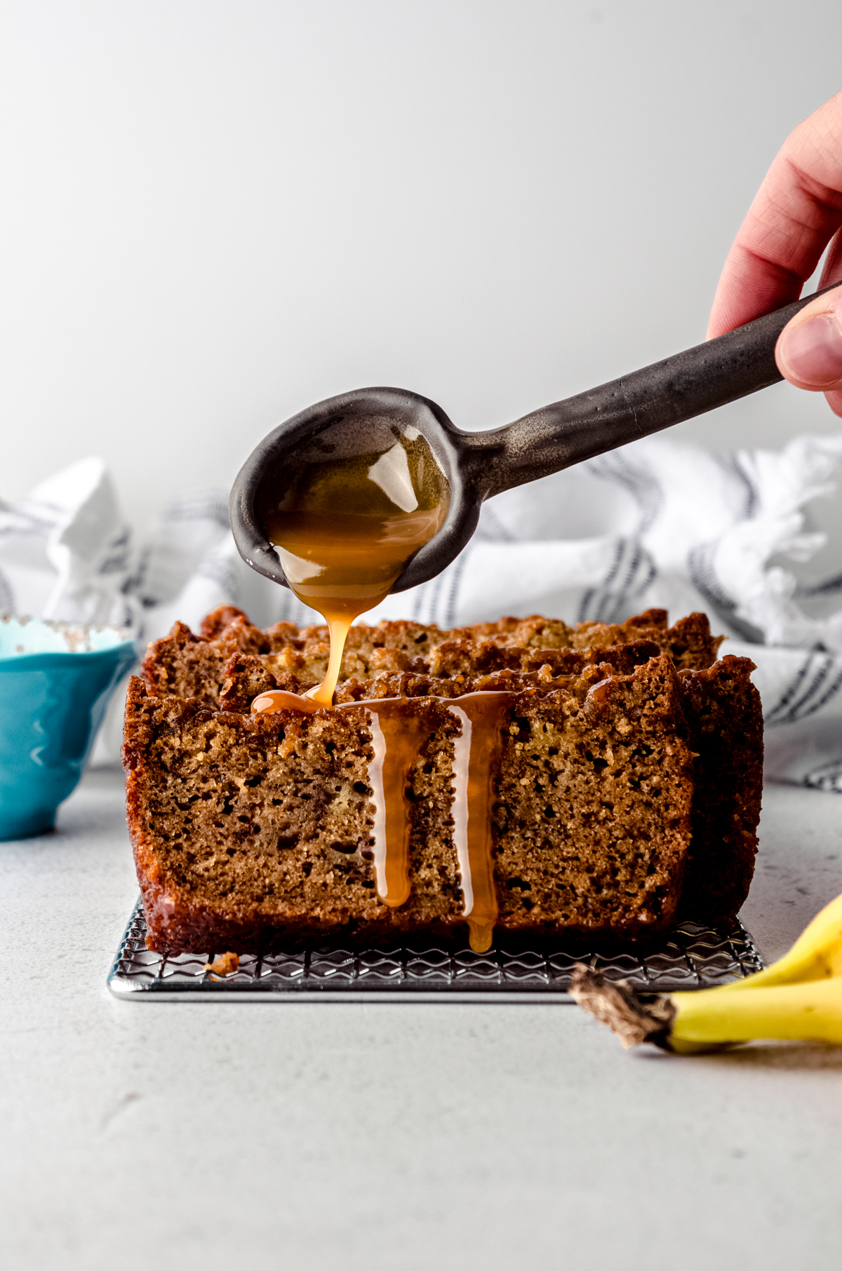 A photo of someone dripping caramel sauce onto a slice of salted caramel banana bread.