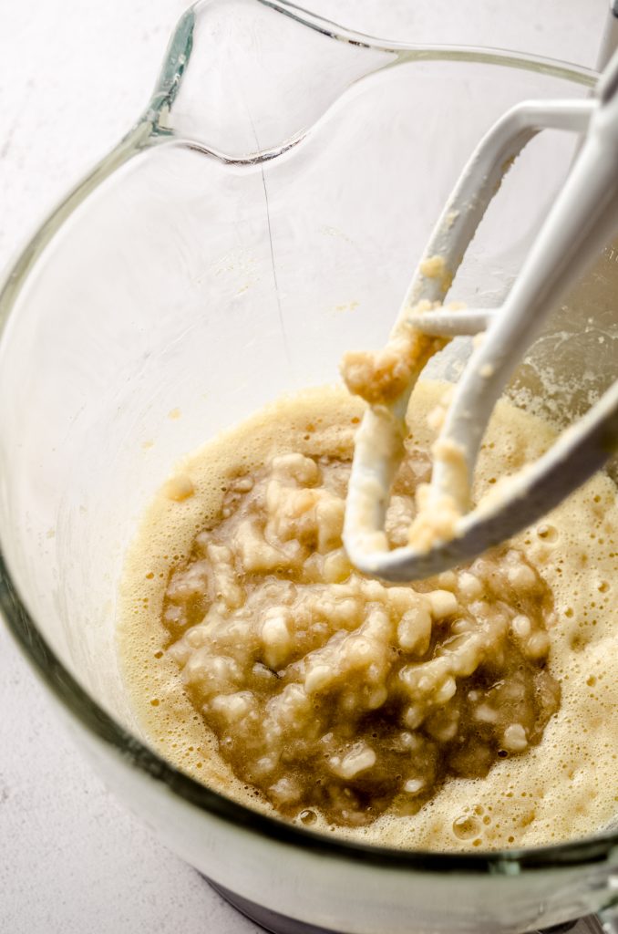 A large glass bowl in a stand mixer with banana bread batter in the bowl.