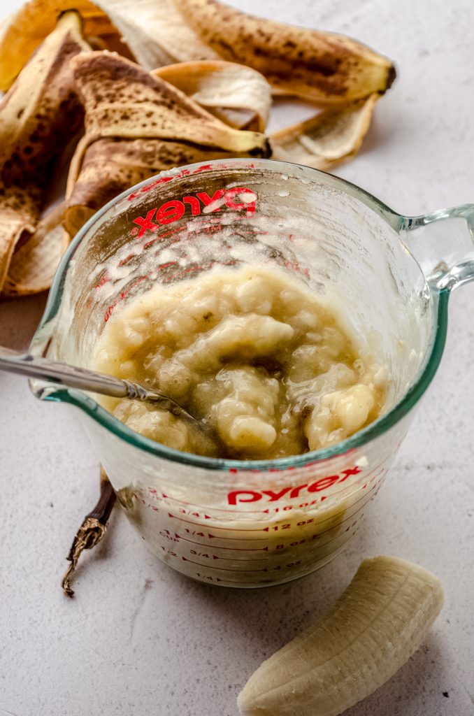 A glass measuring cup with mashed bananas with a fork in it.