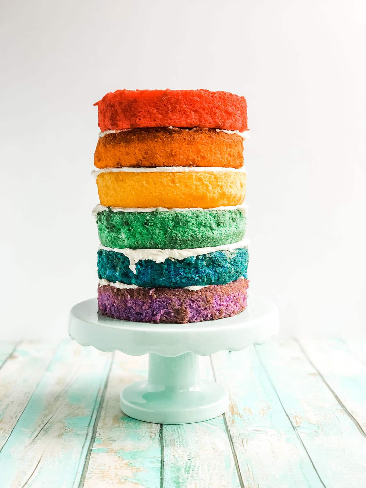 A tall rainbow cake on a cake stand.