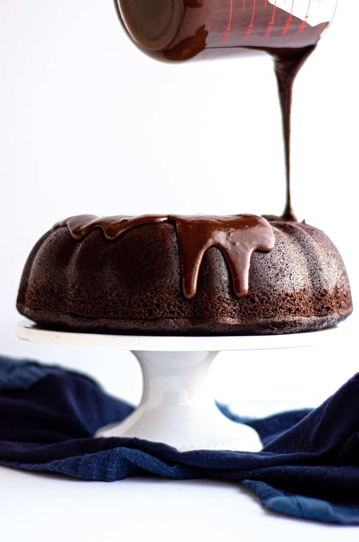 pouring chocolate ganache onto a chocolate bundt cake