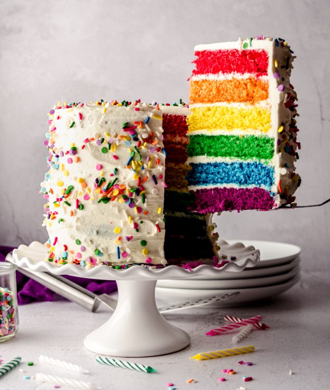 Someone is taking a slice of rainbow layer cake out of the cake with a server.