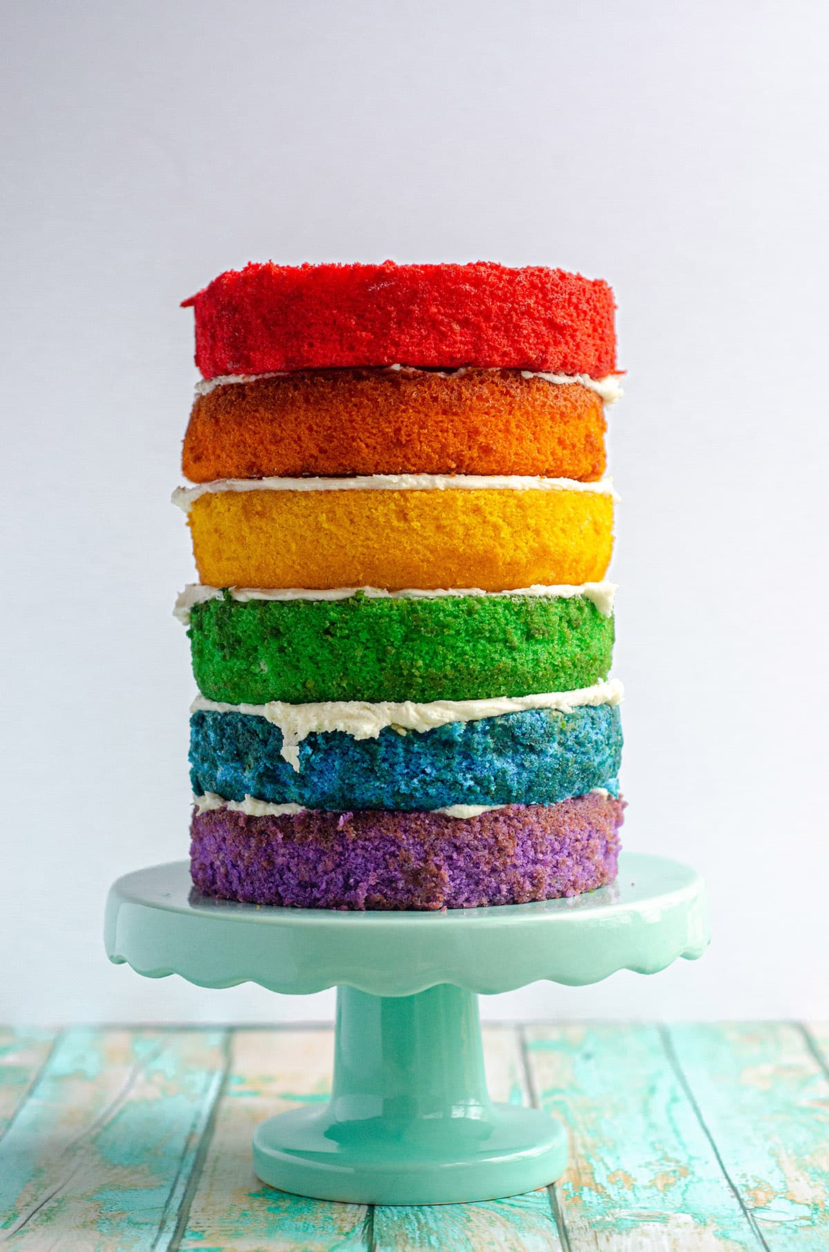 a naked rainbow cake on a cake stand