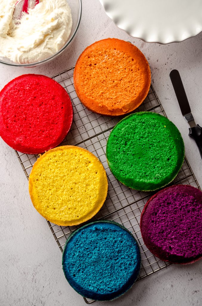 Aerial photos of layers for a rainbow layer cake on a cooling rack that have been trimmed.