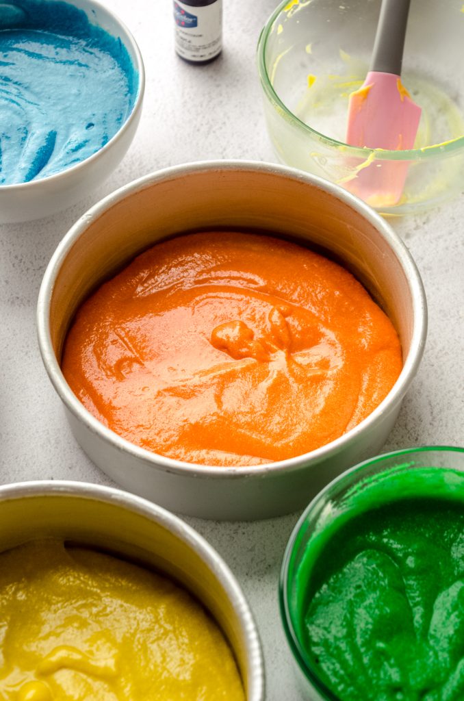 Orange cake batter in a pan ready to bake for the orange layer of a rainbow cake.