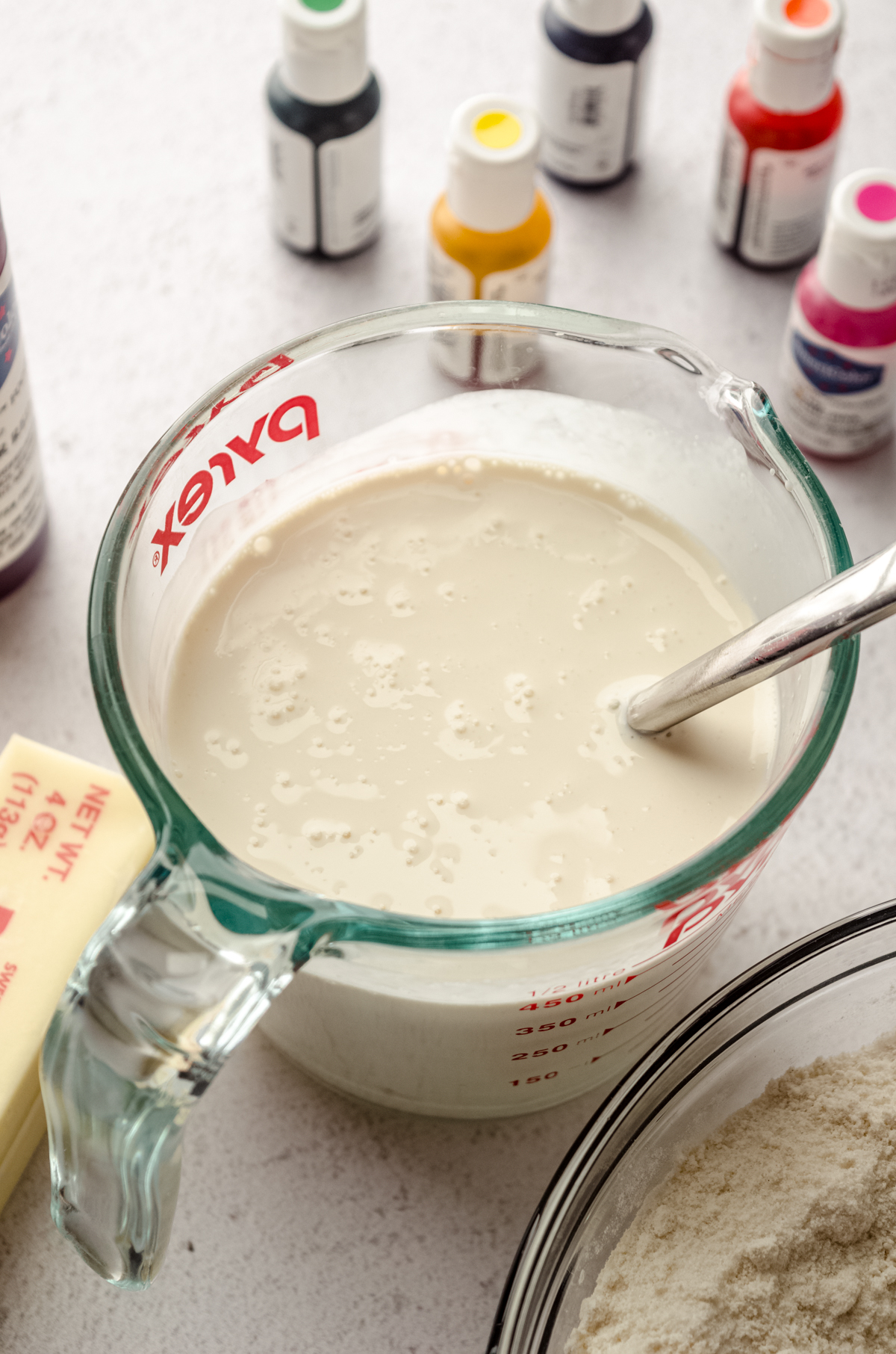 The liquid portion of the ingredients for rainbow layer cake in a large measuring cup with a spatula in it.