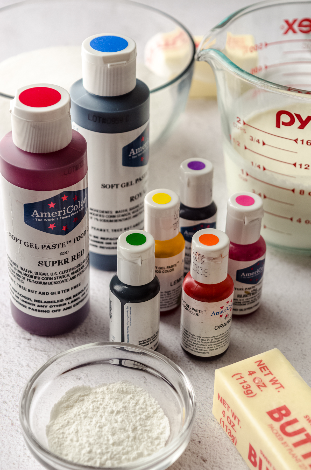 Bottles of gel coloring surrounded by ingredients to make rainbow layer cake.