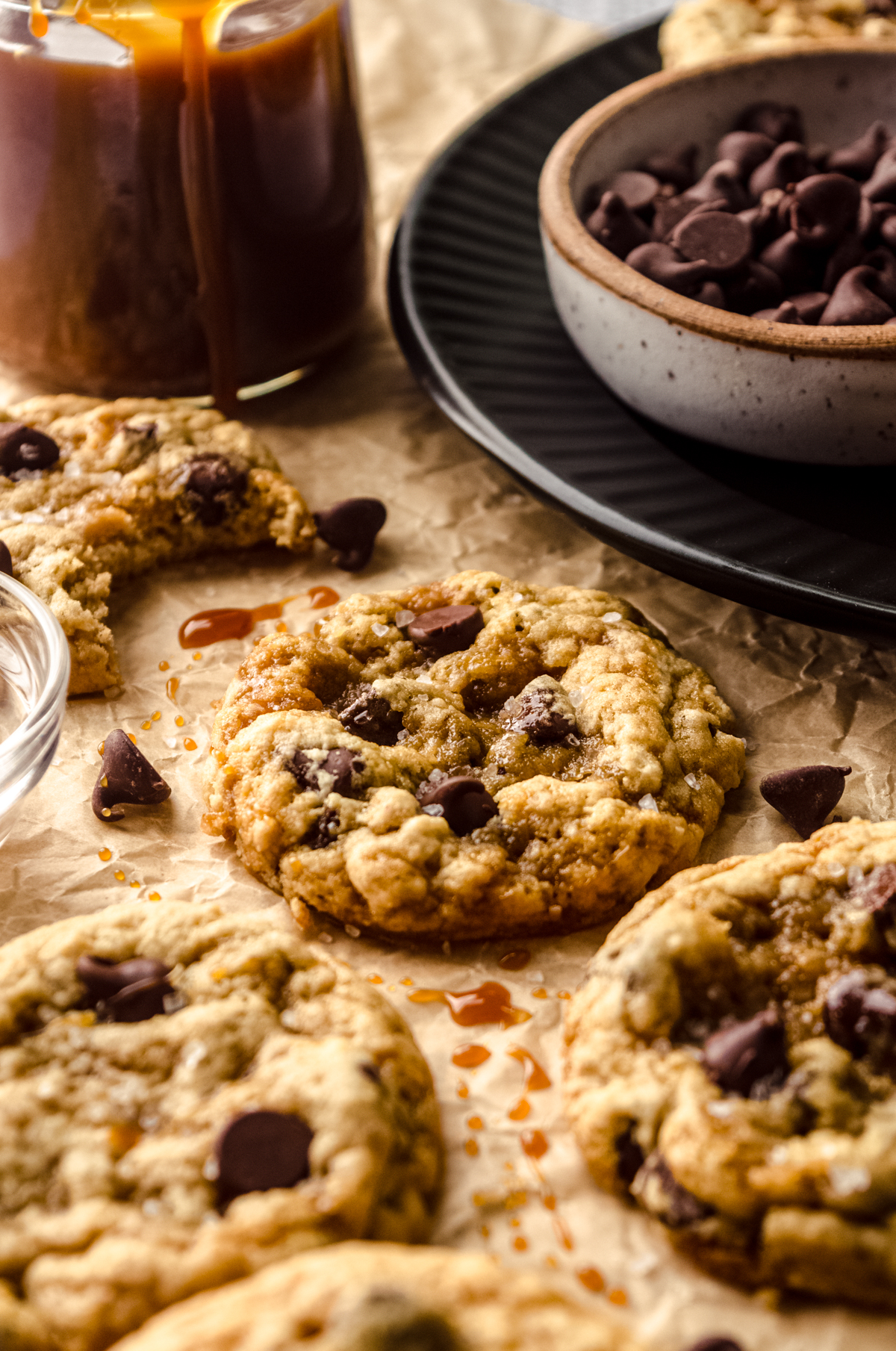 A salted caramel cookie on a piece of parchment paper with caramel sauce and chocolate chips around it.