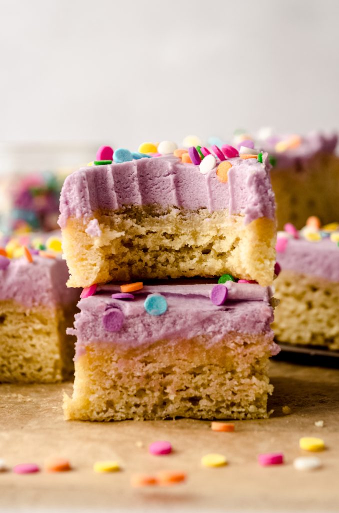 A stack of two frosted sugar cookie bars on a piece of parchment paper and a bite has been taken out of the one on the top.