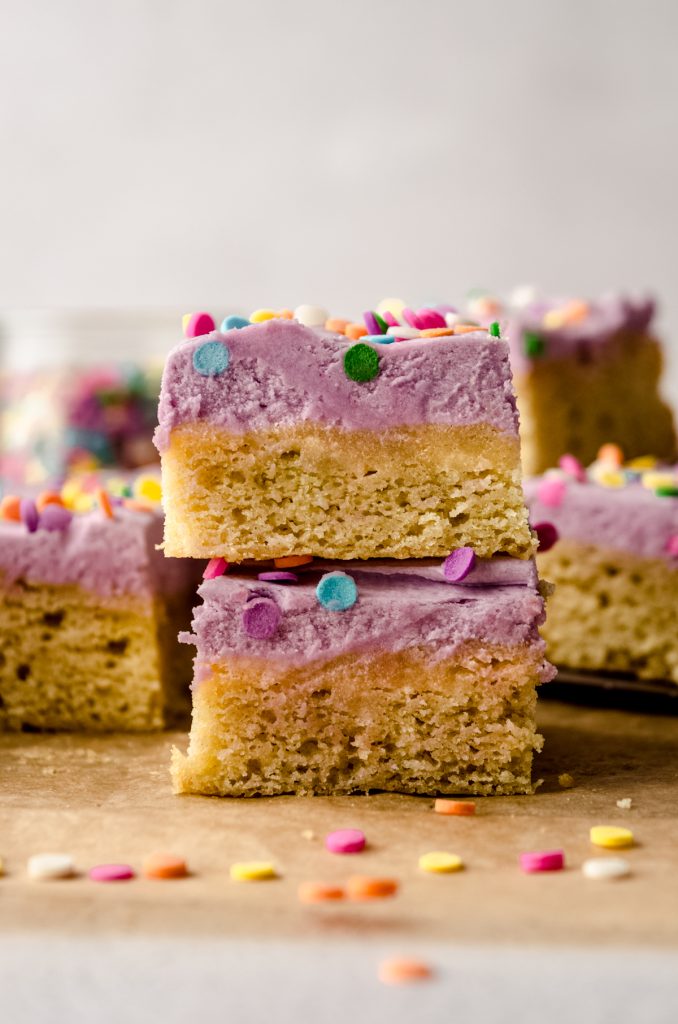 A stack of two frosted sugar cookie bars on a piece of parchment paper.