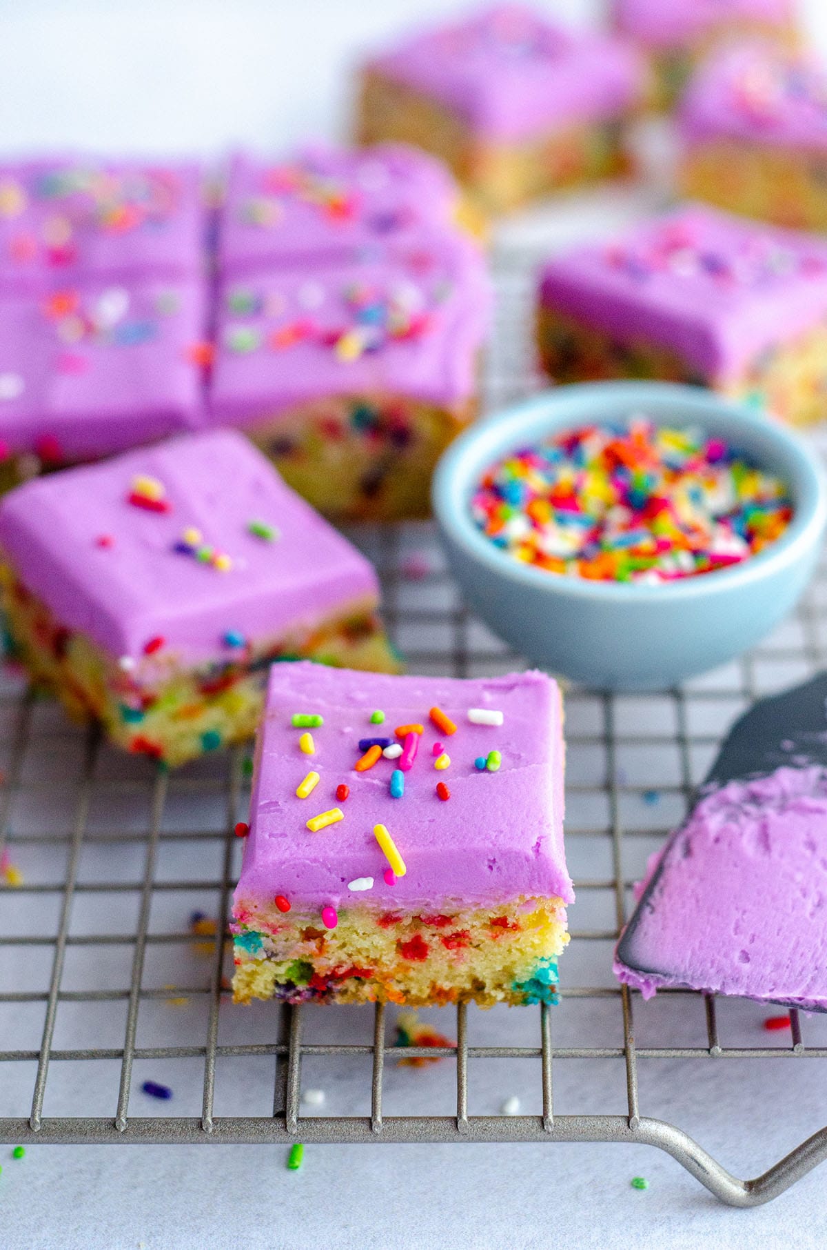 Soft and buttery sugar cookie batter baked in one pan to create easy sugar cookie bars. Top with a colorful buttercream and rainbow sprinkles for an extra pop of color! via @frshaprilflours