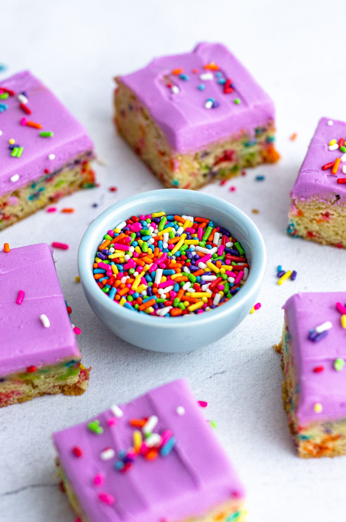 small bowl of rainbow sprinkles surrounded by sugar cookie bars