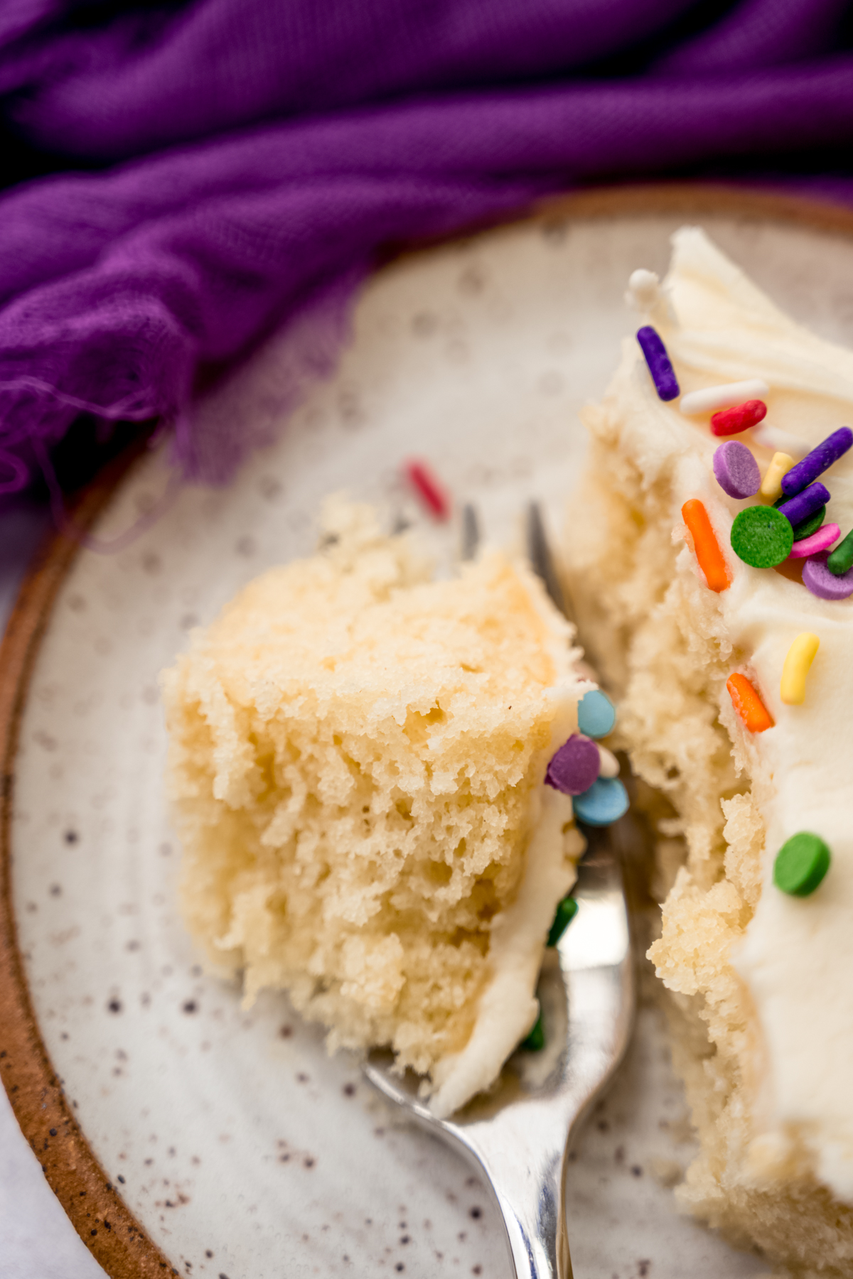 Aerial photo of slice of white sheet cake on a plate with a fork and a bite taken out of the cake.