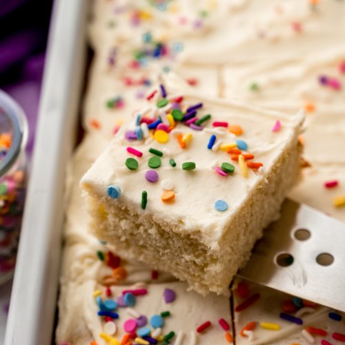 A photo of someone lifting a slice of white sheet cake out of a pan with a server.