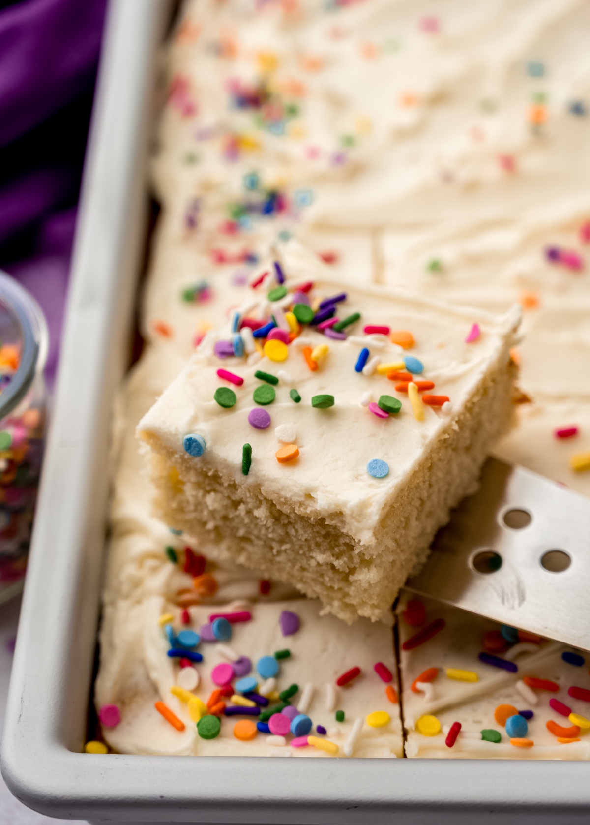 A photo of someone lifting a slice of white sheet cake out of a pan with a server.