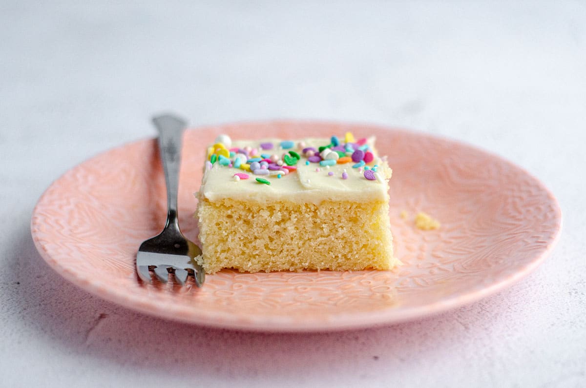slice of white sheet cake on a pink plate with a fork