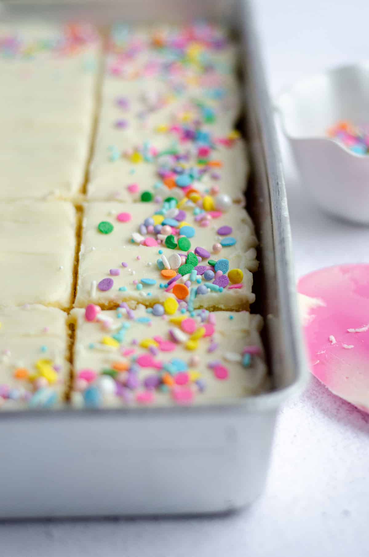 white sheet cake sliced and in a baking pan with colorful sprinkles