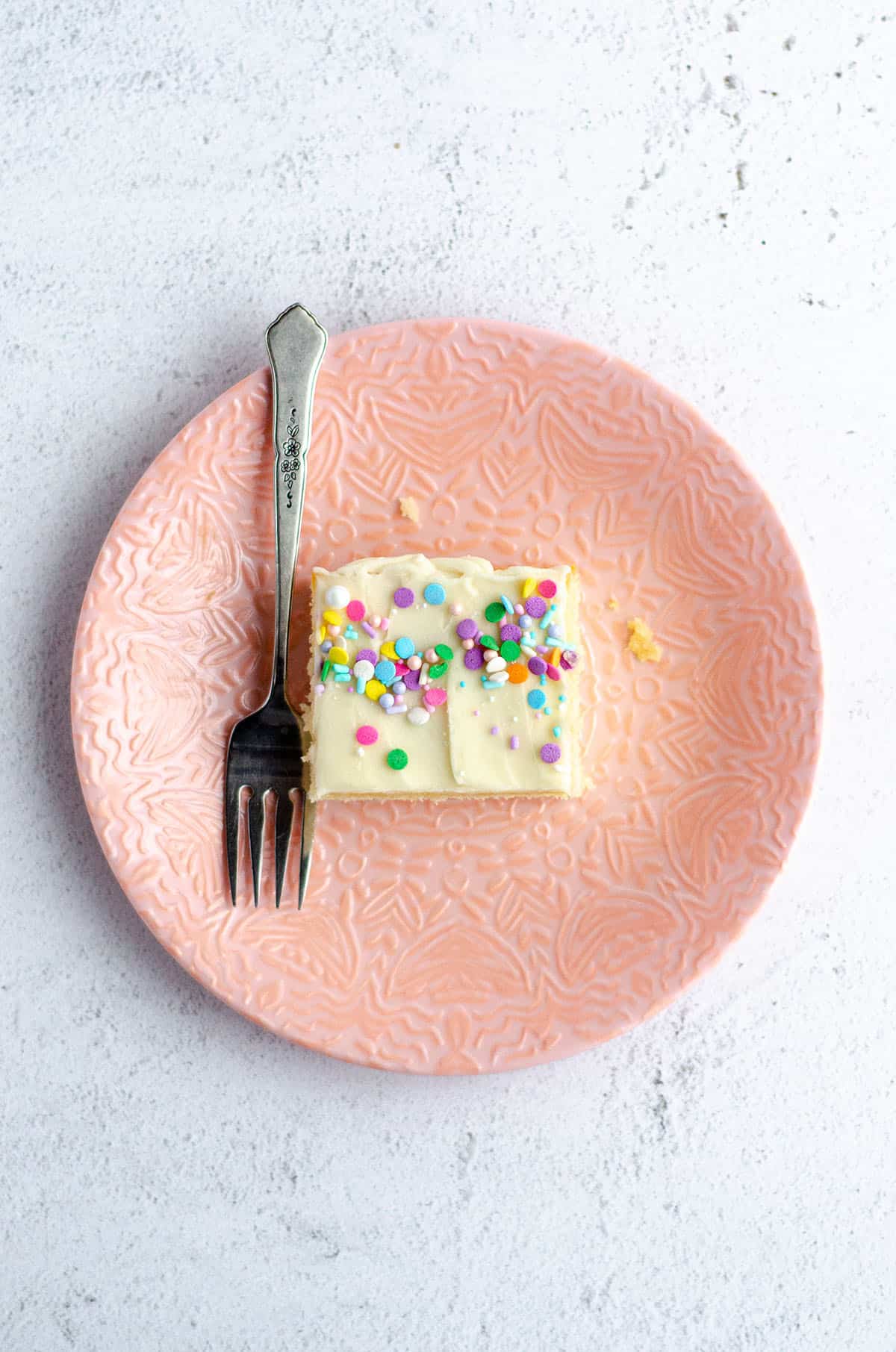 aerial shot of white sheet cake slice on a pink plate with a fork