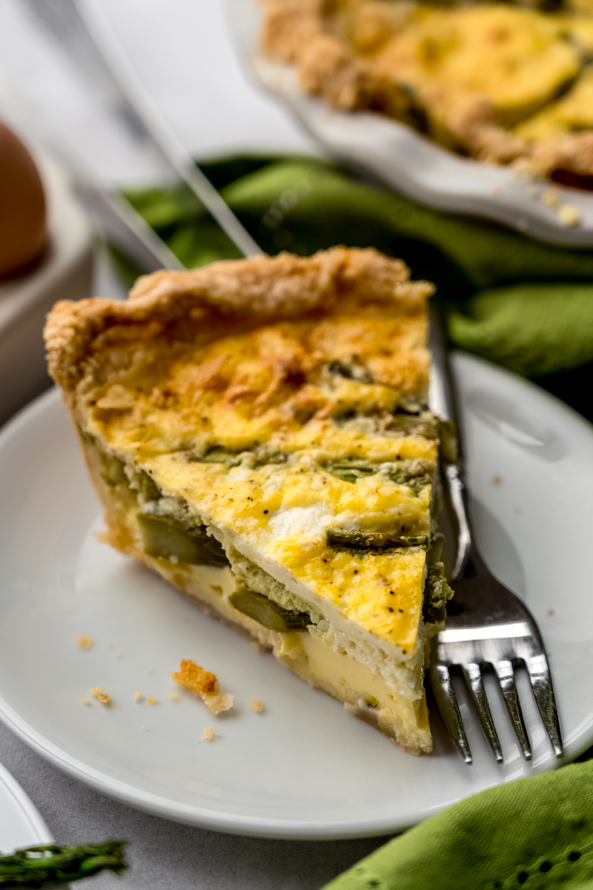 A slice of asparagus quiche on a plate with a fork.