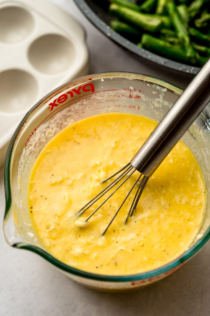 The mixture for a quiche in a large glass measuring cup with a whisk.