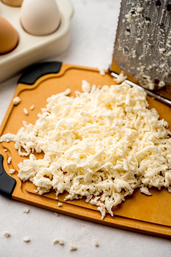 Shredded mozzarella cheese on a cutting board.