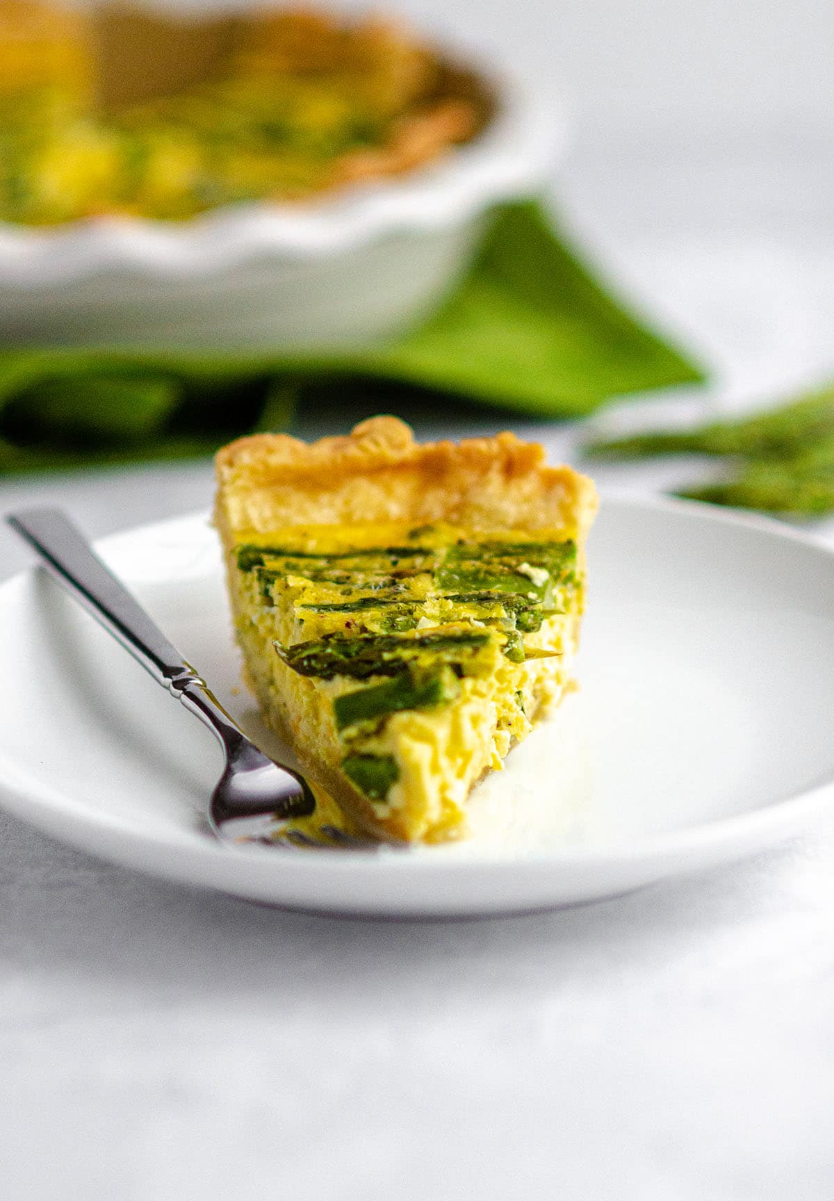 slice of asparagus quiche on a white plate with a fork