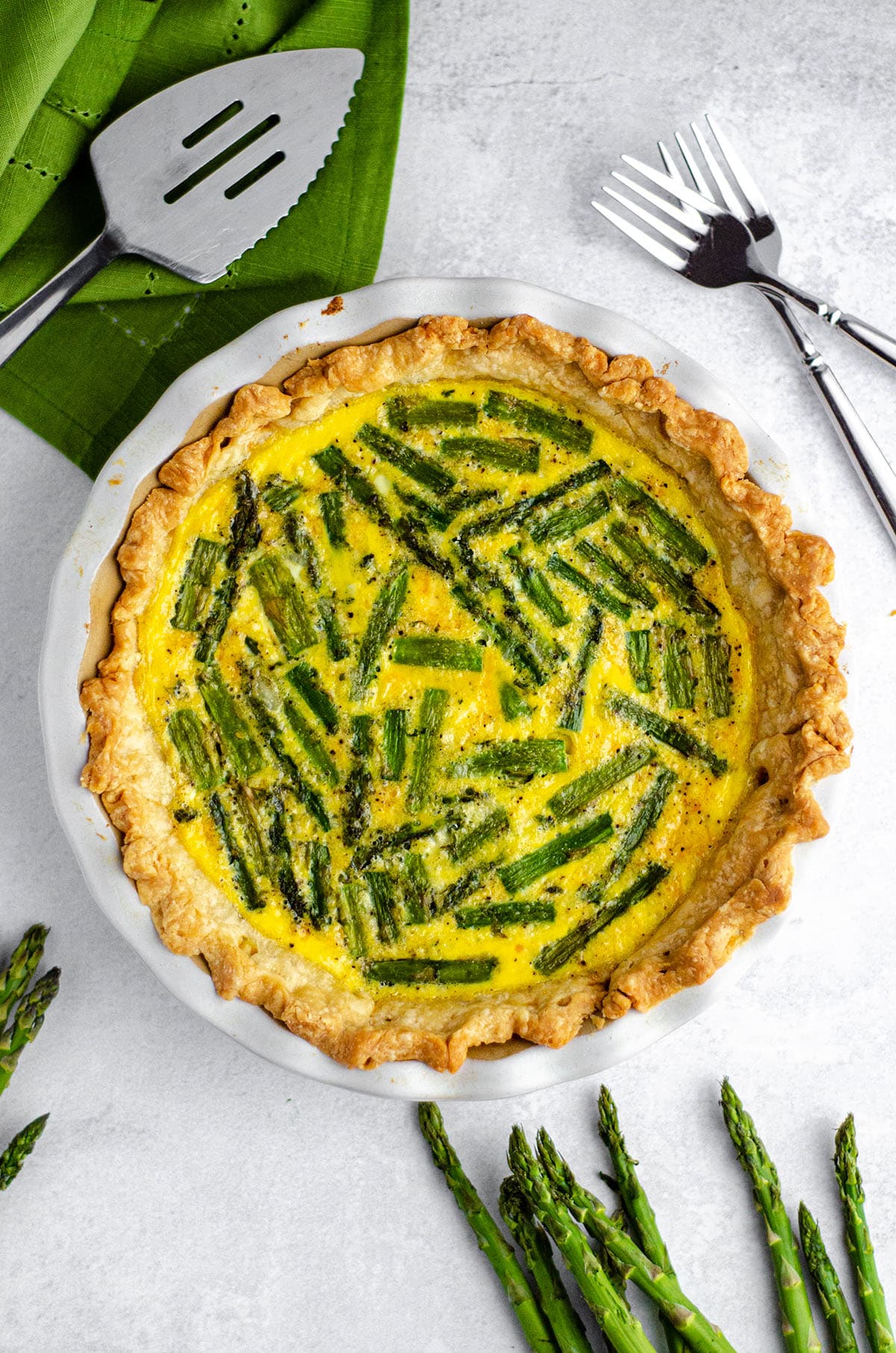 aerial photo of asparagus quiche in a pie plate with forks and a server around it