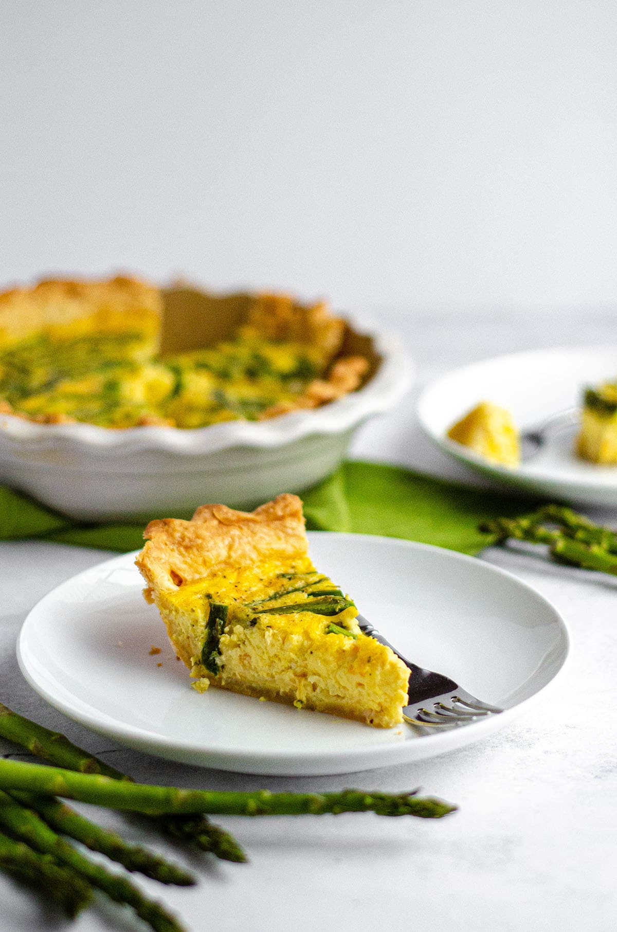 slice of asparagus quiche on a white plate with a fork