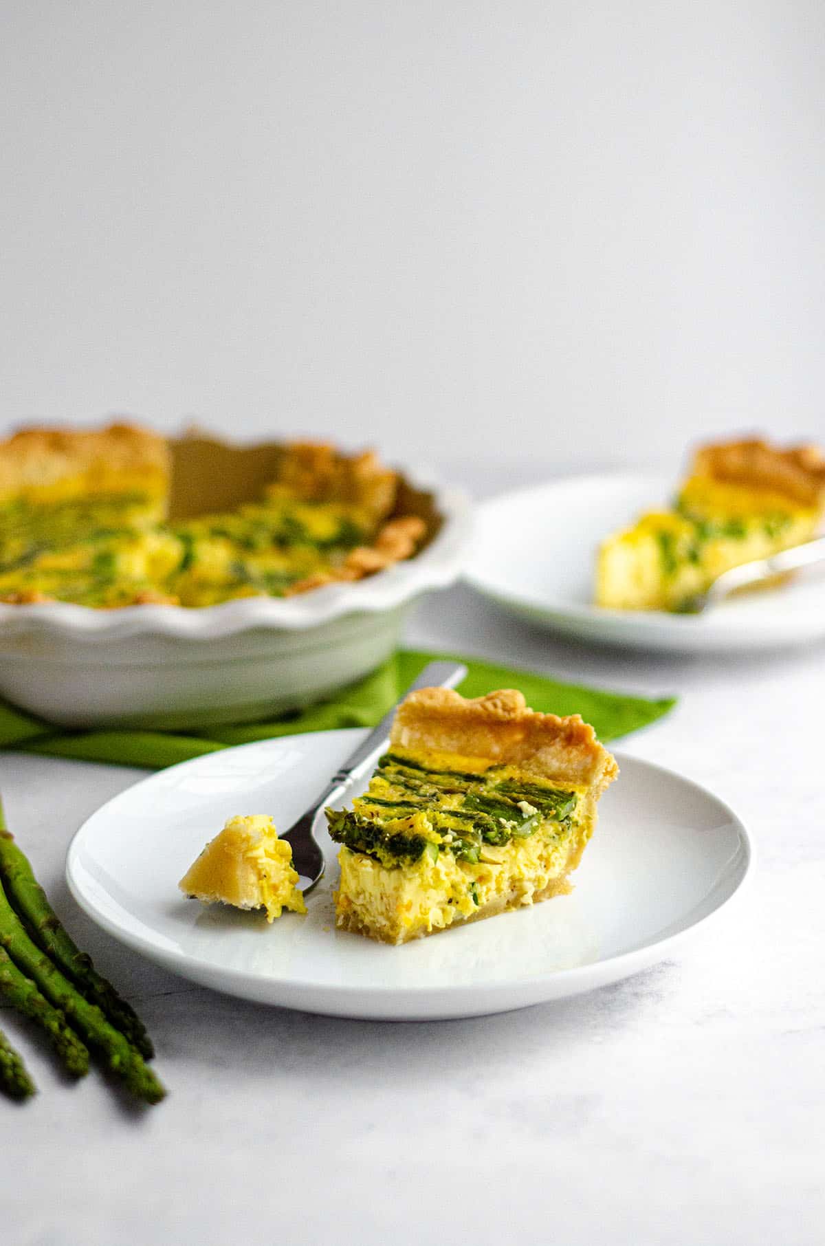 slice of asparagus quiche on a white plate with a fork and a bite taken out of the slice