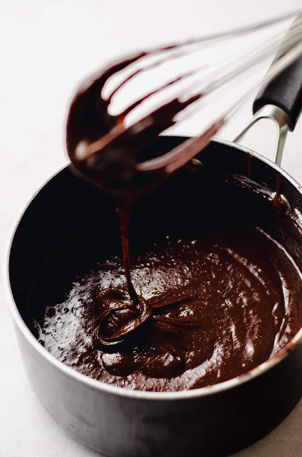 a whisk pulling brownie batter out of a saucepan before pouring it into a baking pan
