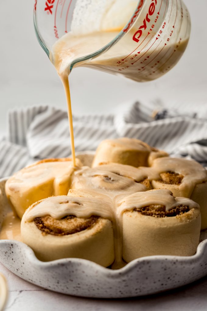 Someone is pouring a mixture of heavy cream and caramel onto a baking dish of cinnamon rolls before baking.