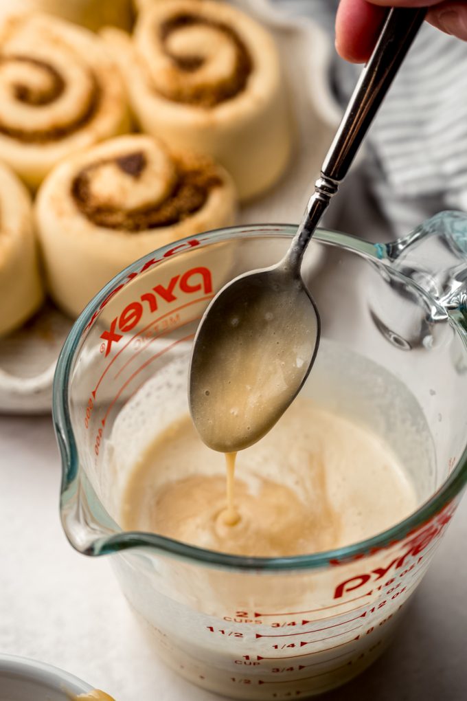 Someone is stirring a measuring cup of heavy cream and caramel sauce with a spoon.