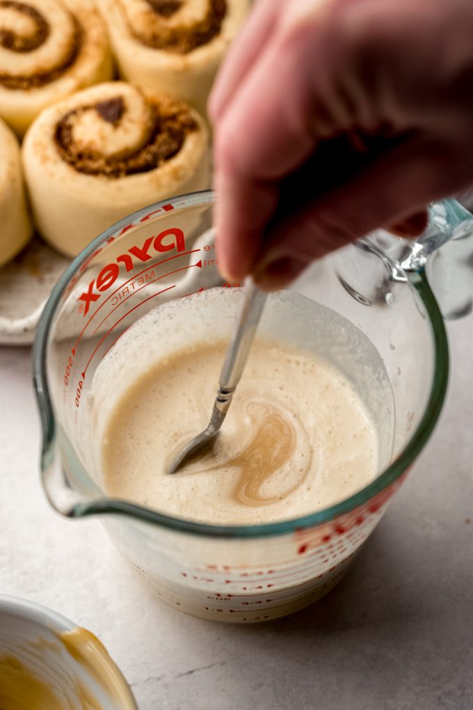 Someone is stirring a measuring cup of heavy cream and caramel sauce with a spoon.